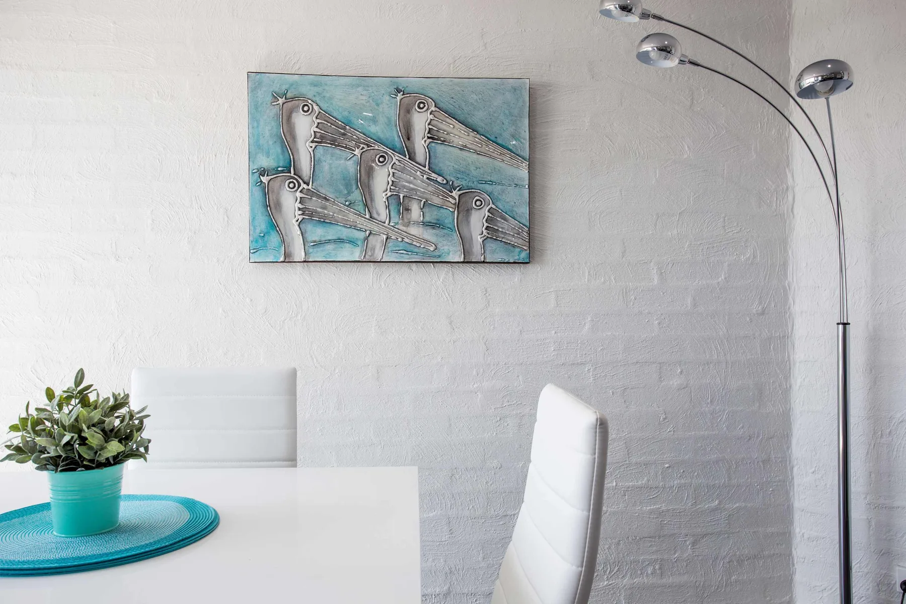 A bright dining area with white seating, a table, and wall art.