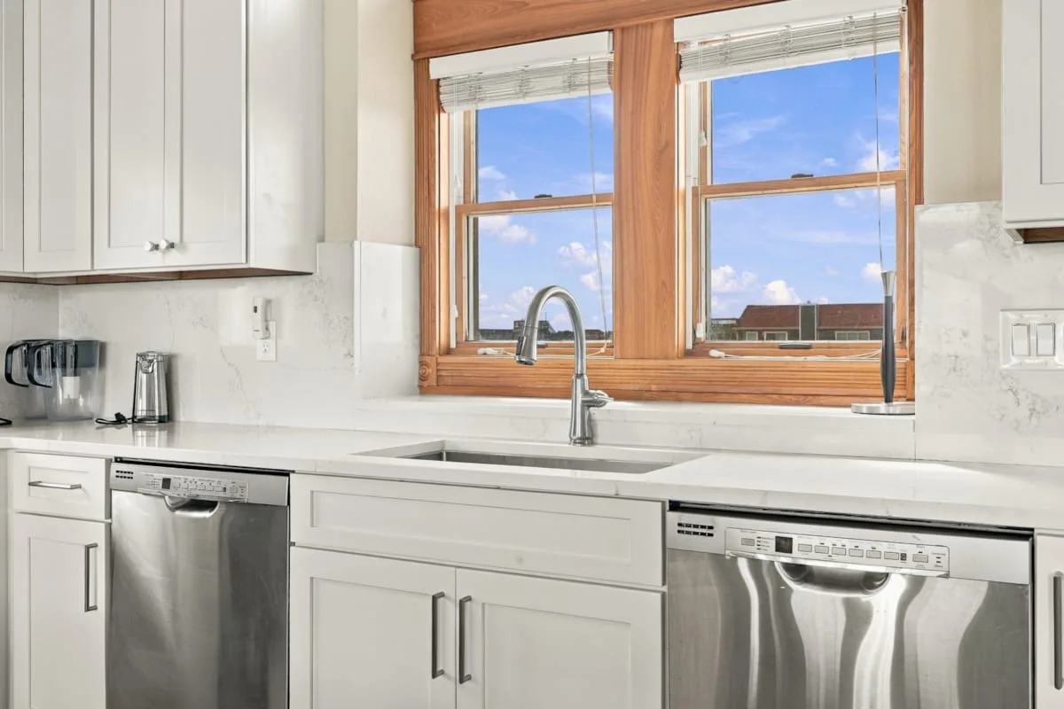 Una cocina luminosa con un fregadero bajo dos ventanas grandes.
