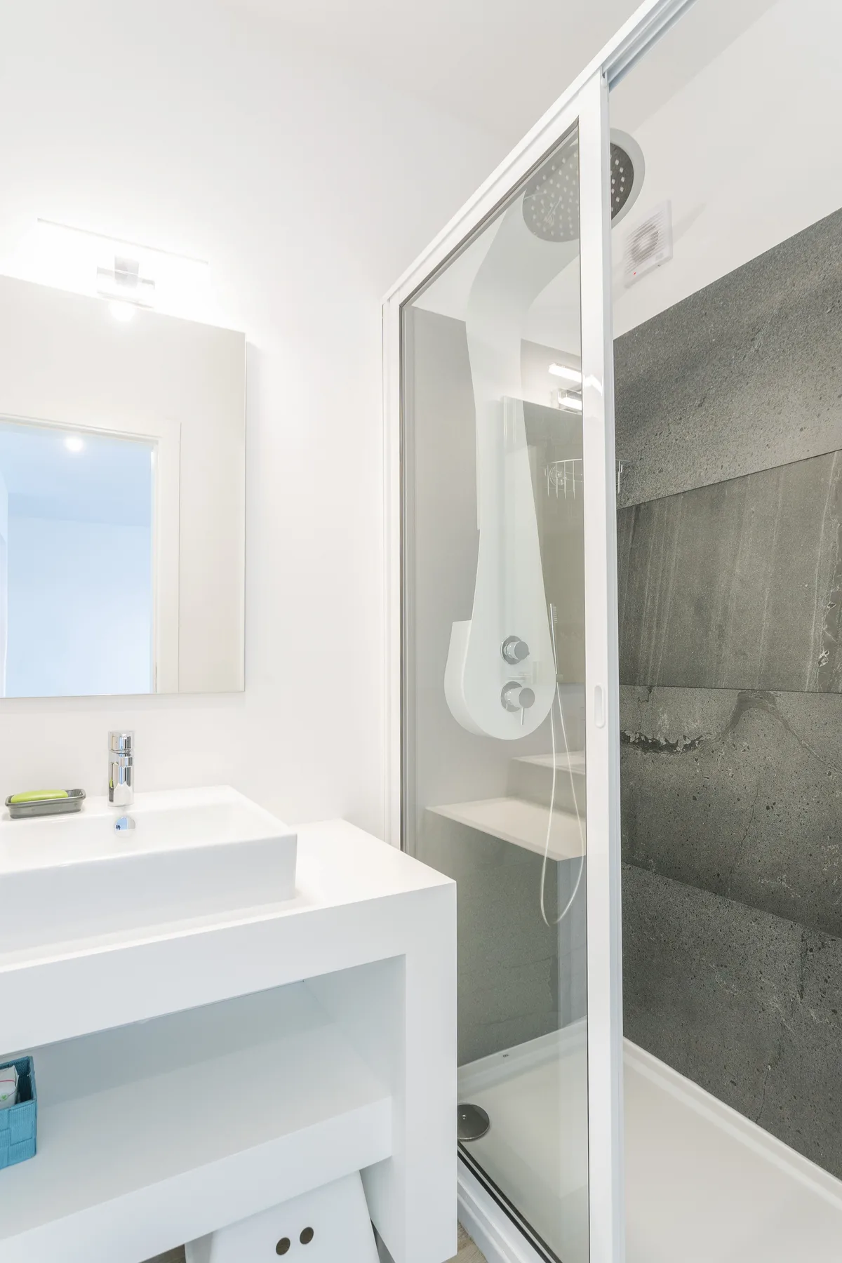 A bright bathroom has a white sink beside a glass-enclosed shower.