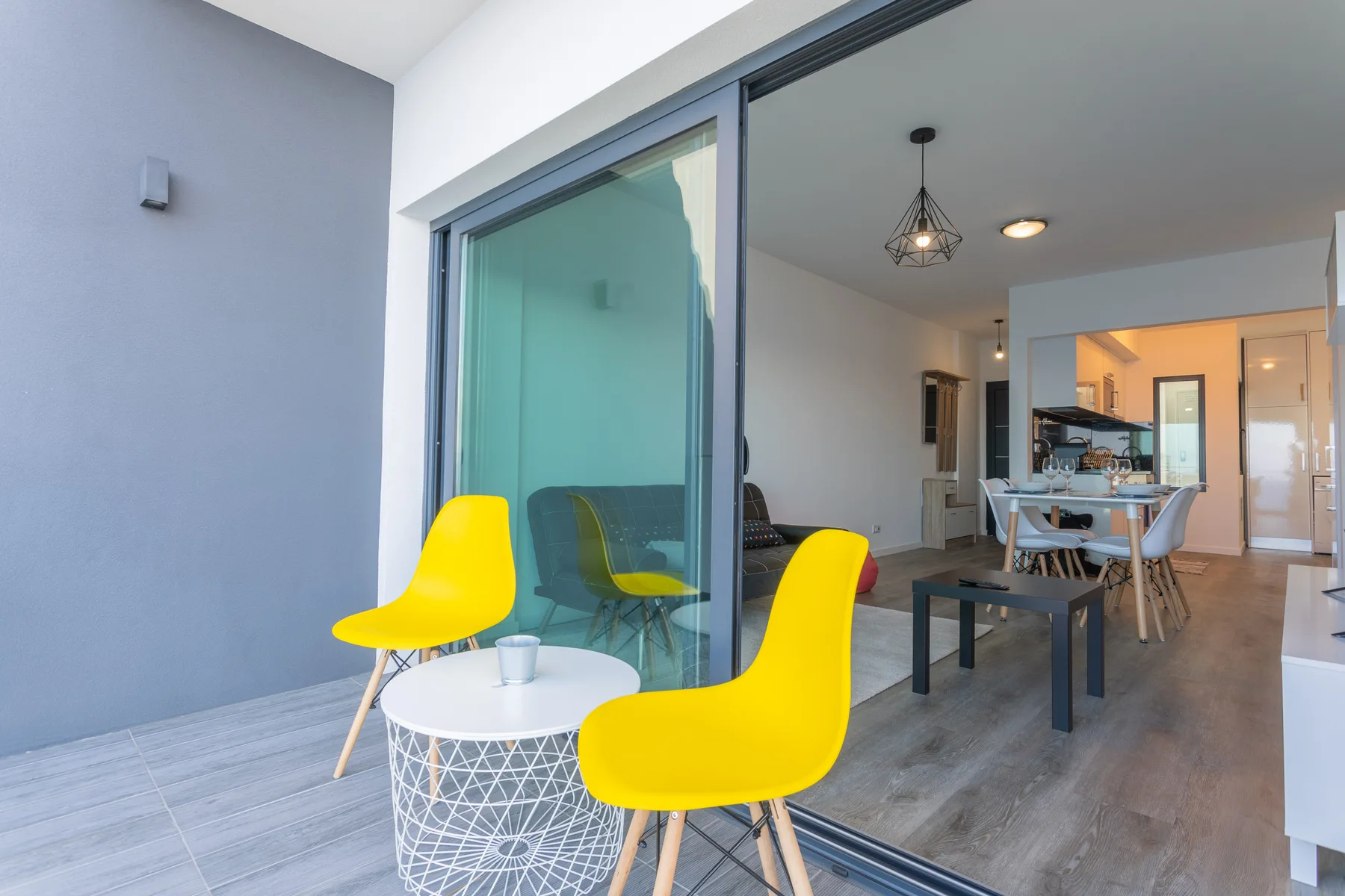 Una sala de estar y comedor se abre a un balcón con asientos amarillos y una mesa pequeña.