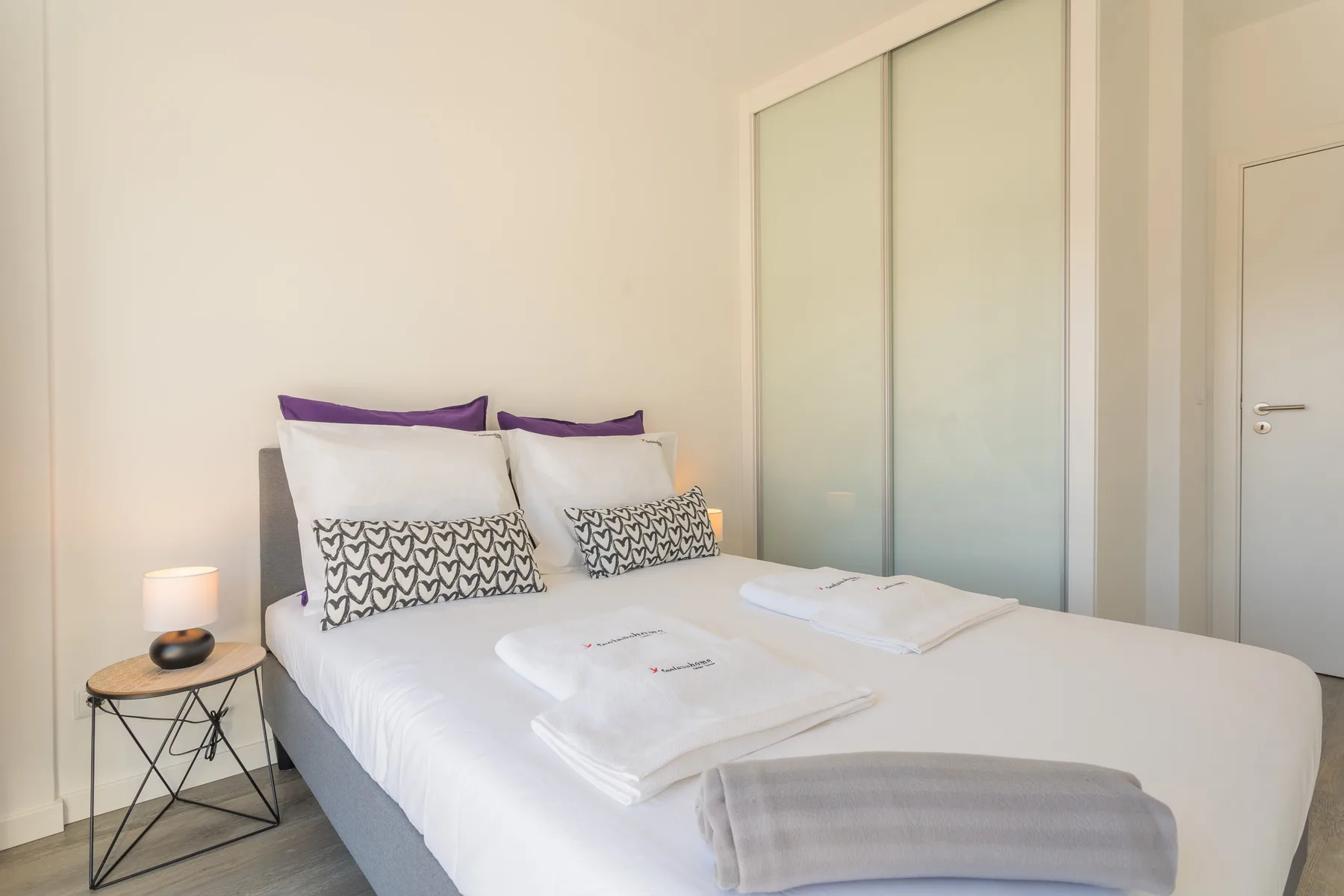 Un dormitorio luminoso con una cama bien hecha y toallas dobladas.