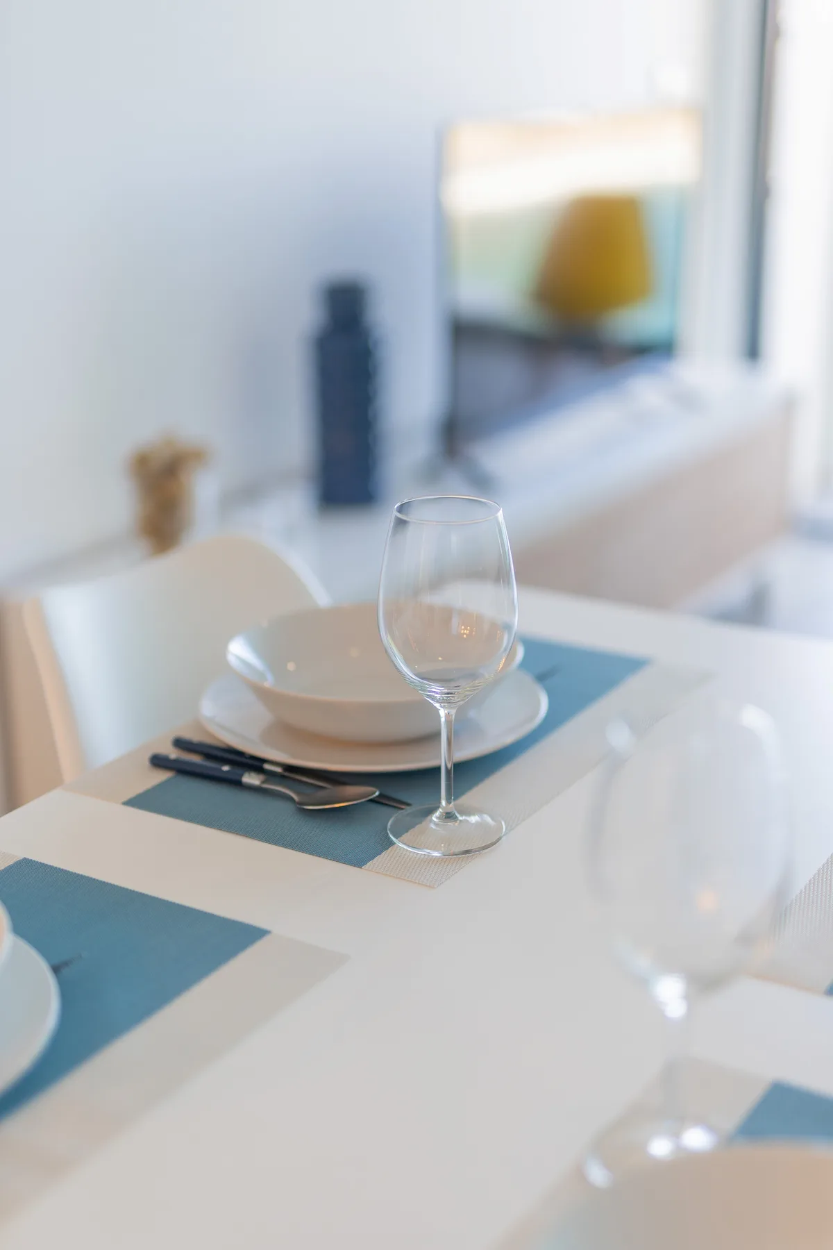 Una mesa de comedor está puesta con platos, cubiertos y copas transparentes.