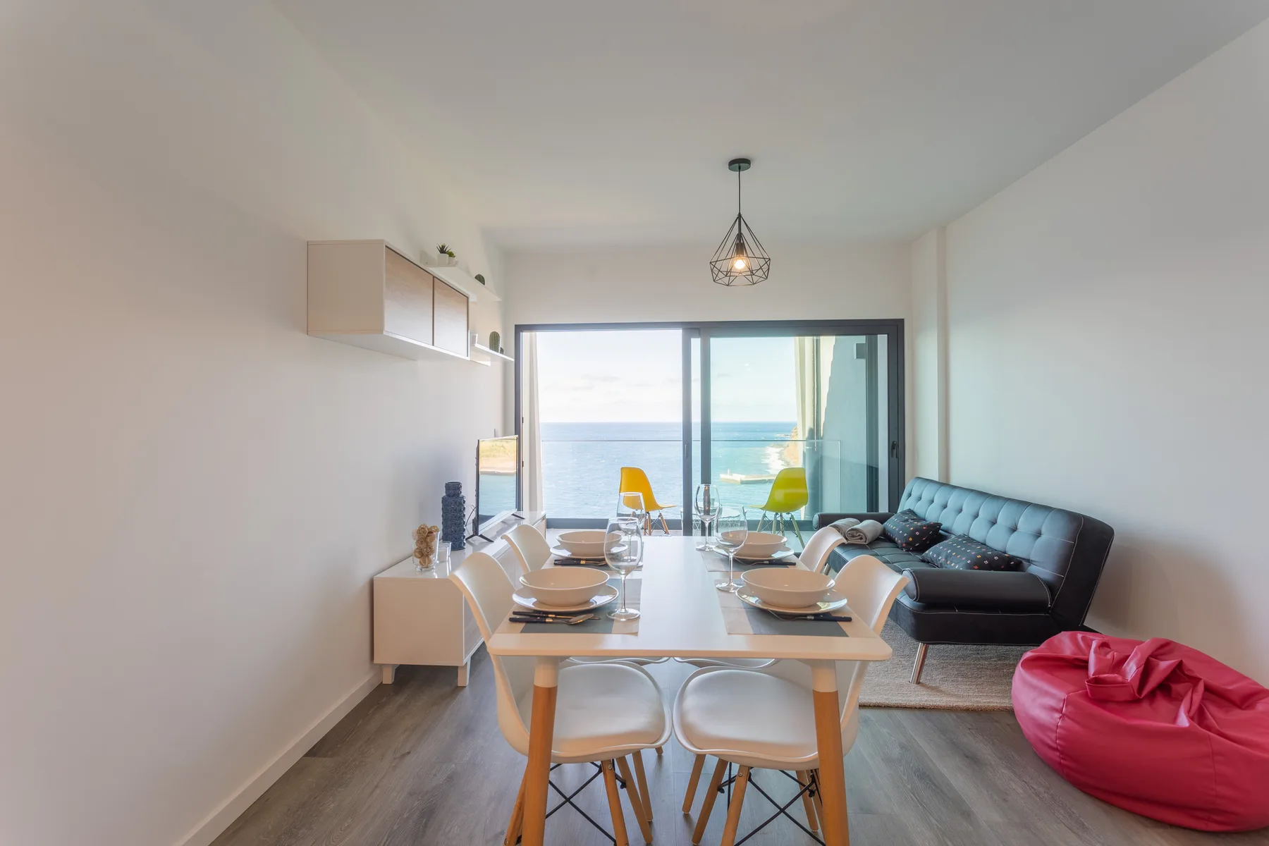 A bright dining and living area opens onto a balcony with an ocean view.