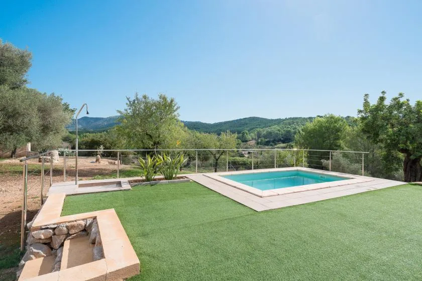 An outdoor swimming pool sits beside a broad green lawn with wooded hills beyond.