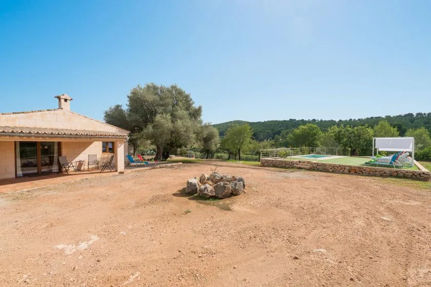 A spacious outdoor yard with a low house, trees, and a pool in the background.