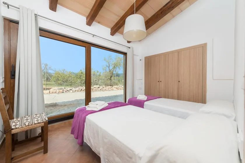 A bright bedroom with two beds beside a large window overlooking trees.