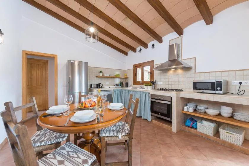 A kitchen and dining area with a wooden table set beneath exposed ceiling beams.