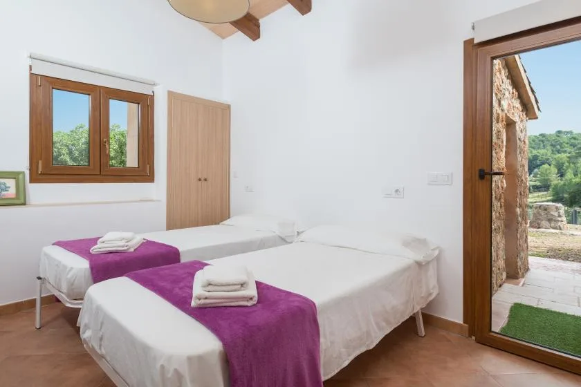 A bright bedroom with twin beds dressed in white linens and purple runners.