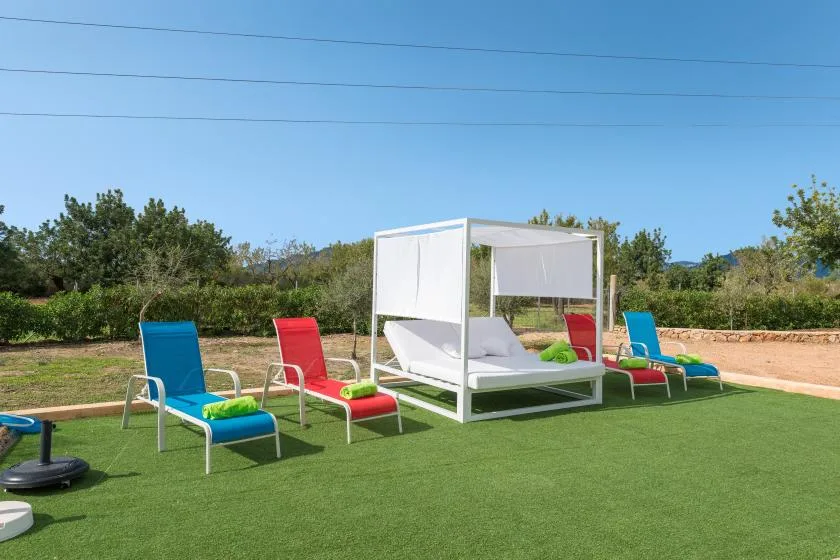 Outdoor seating area with colorful chairs and a white canopy daybed on artificial grass.