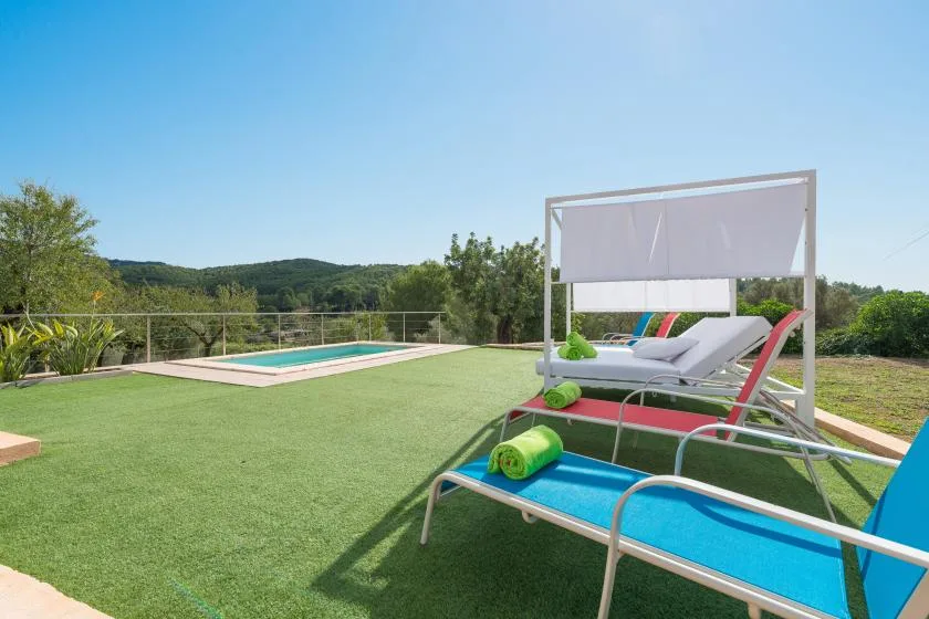 An outdoor poolside seating area has colorful lounge chairs on a grassy terrace.