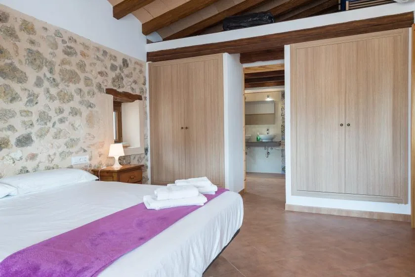 A bedroom with a bed, built-in wardrobes, and a stone wall.