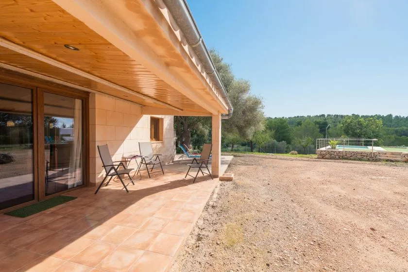 A paved patio beside a house overlooks an open yard and distant greenery.