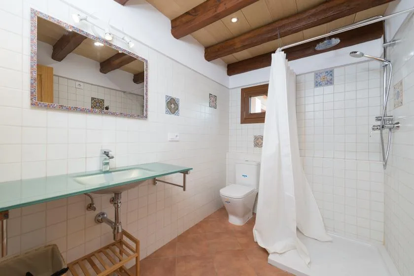 A tiled bathroom with a glass counter, toilet, and curtained shower.