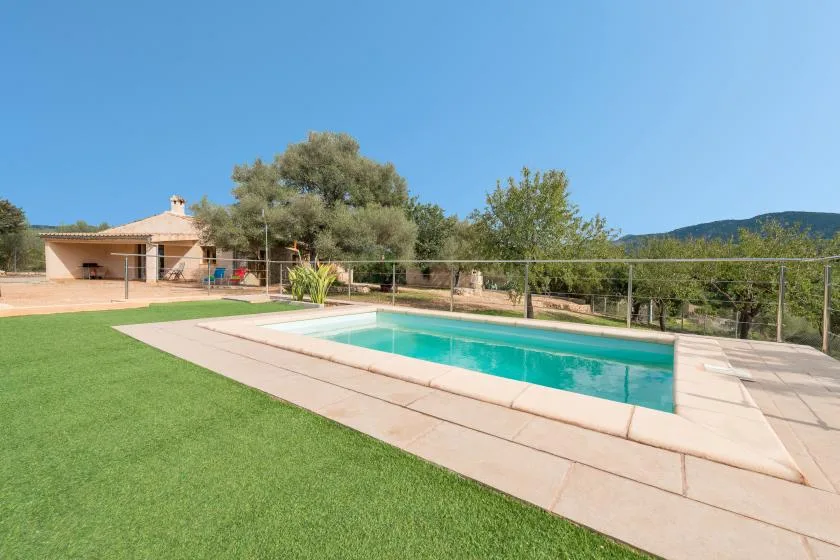 An outdoor swimming pool is surrounded by a paved deck and green lawn.