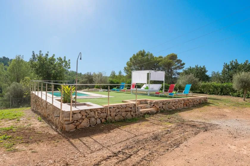 An outdoor swimming pool and patio sit on a raised stone platform surrounded by trees.