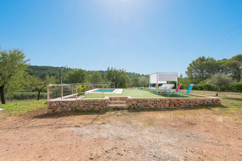 An outdoor swimming pool sits on a raised stone terrace beside a grassy lawn.