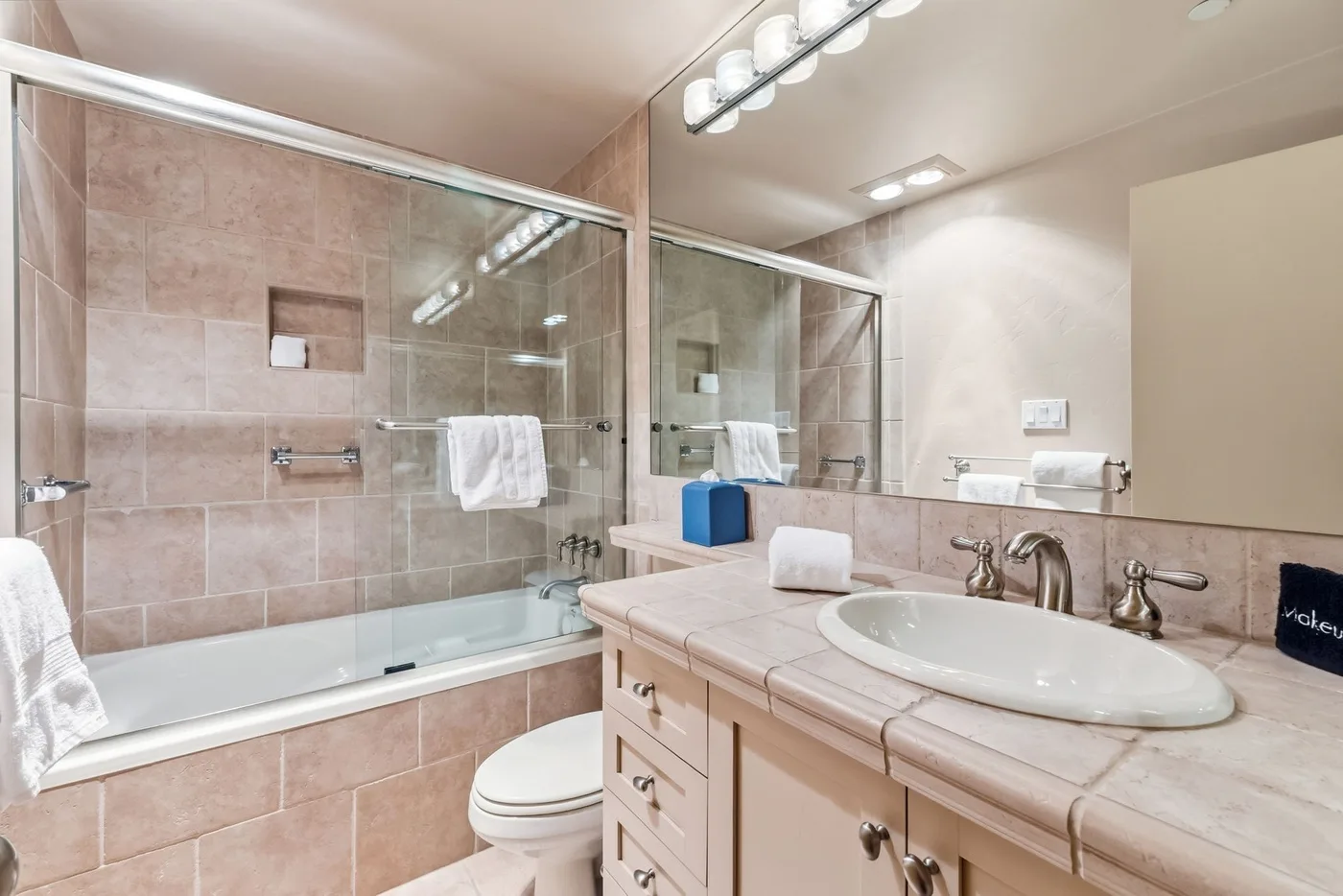 Un baño con bañera de mampara de vidrio, lavabo y un espejo grande.