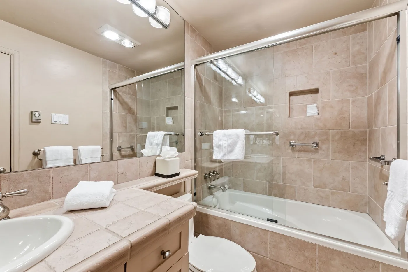Un baño alicatado con bañera, mampara de vidrio y lavabo.