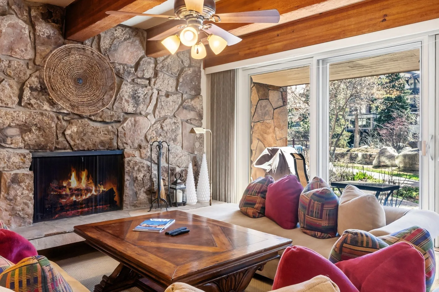 Una sala de estar con chimenea de piedra, mesa de centro y asientos junto a grandes ventanas.