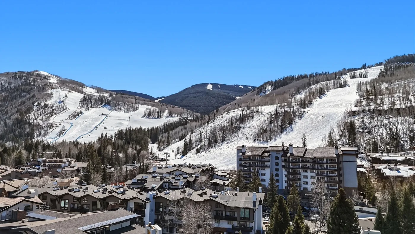 Laderas de esquí cubiertas de nieve se alzan detrás de un pueblo de montaña bajo un cielo despejado.