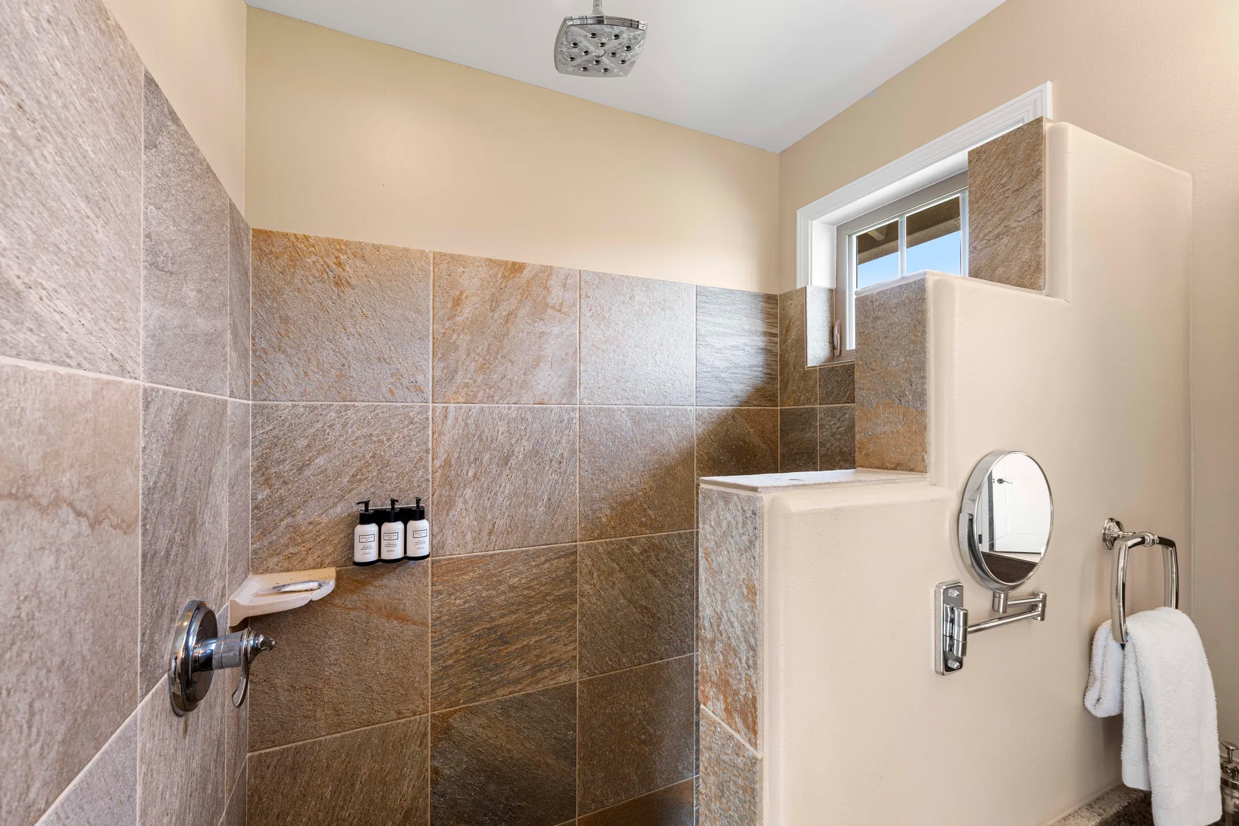 A tiled bathroom shower area with a small window and wall-mounted fixtures.