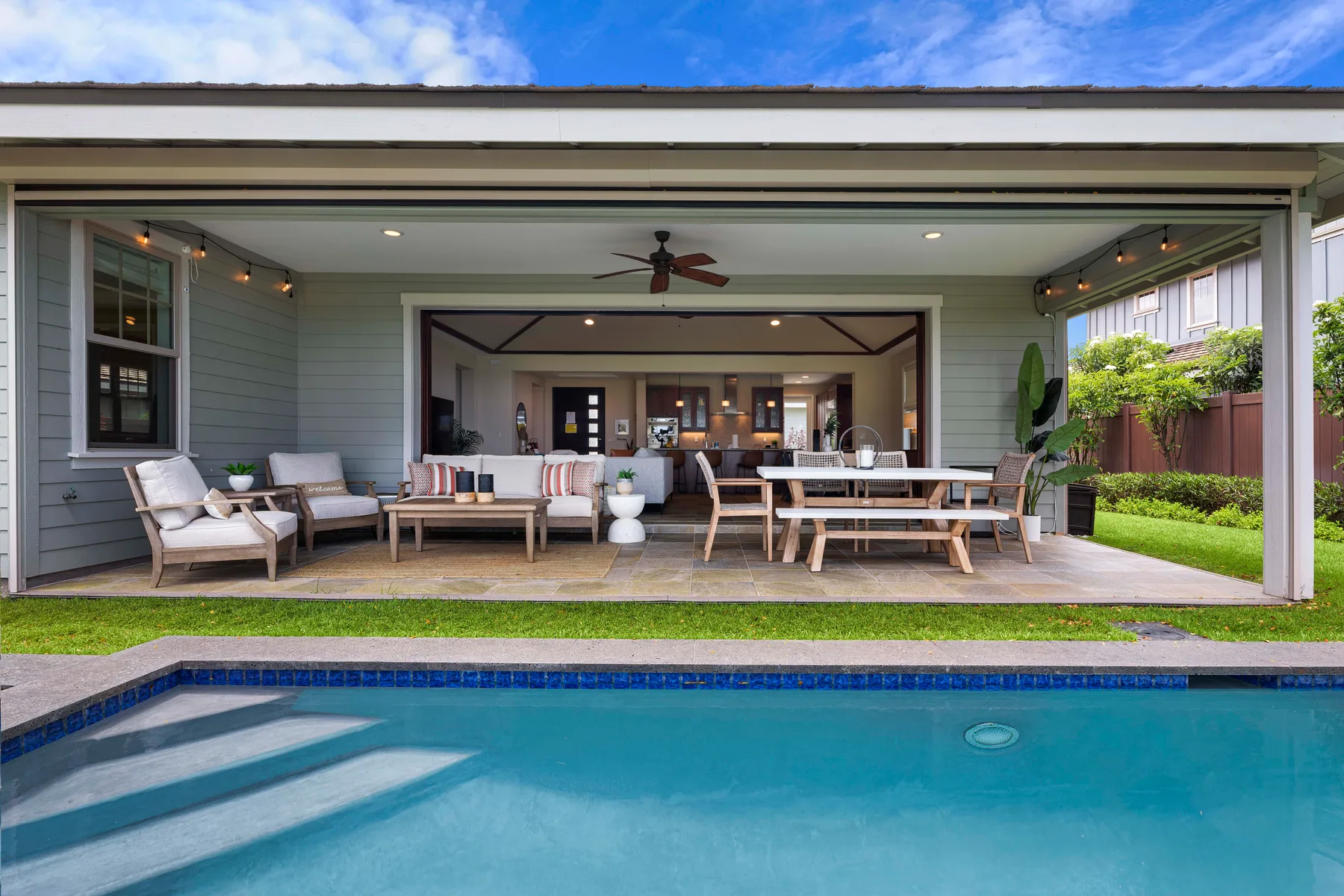 A covered patio with outdoor seating and a dining table opens onto a swimming pool.