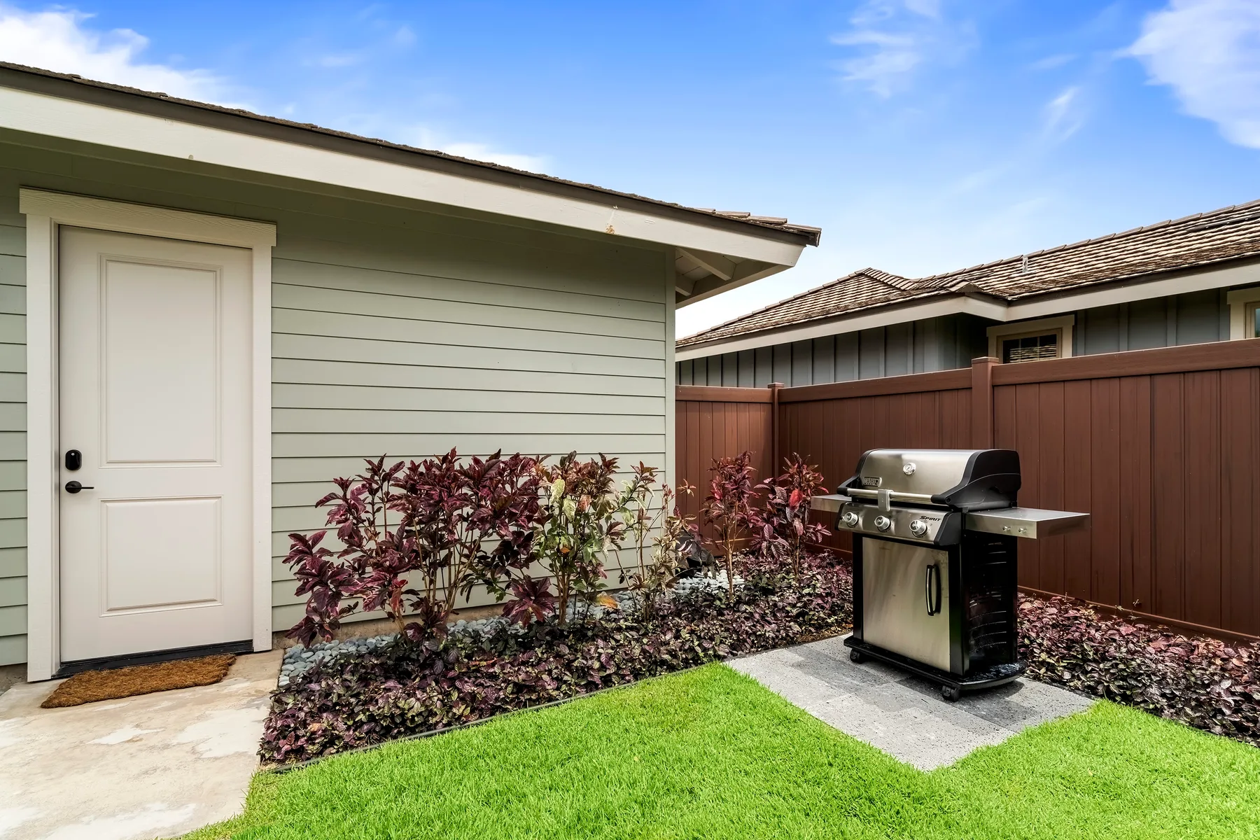 An outdoor patio area has a barbecue grill beside a small lawn.