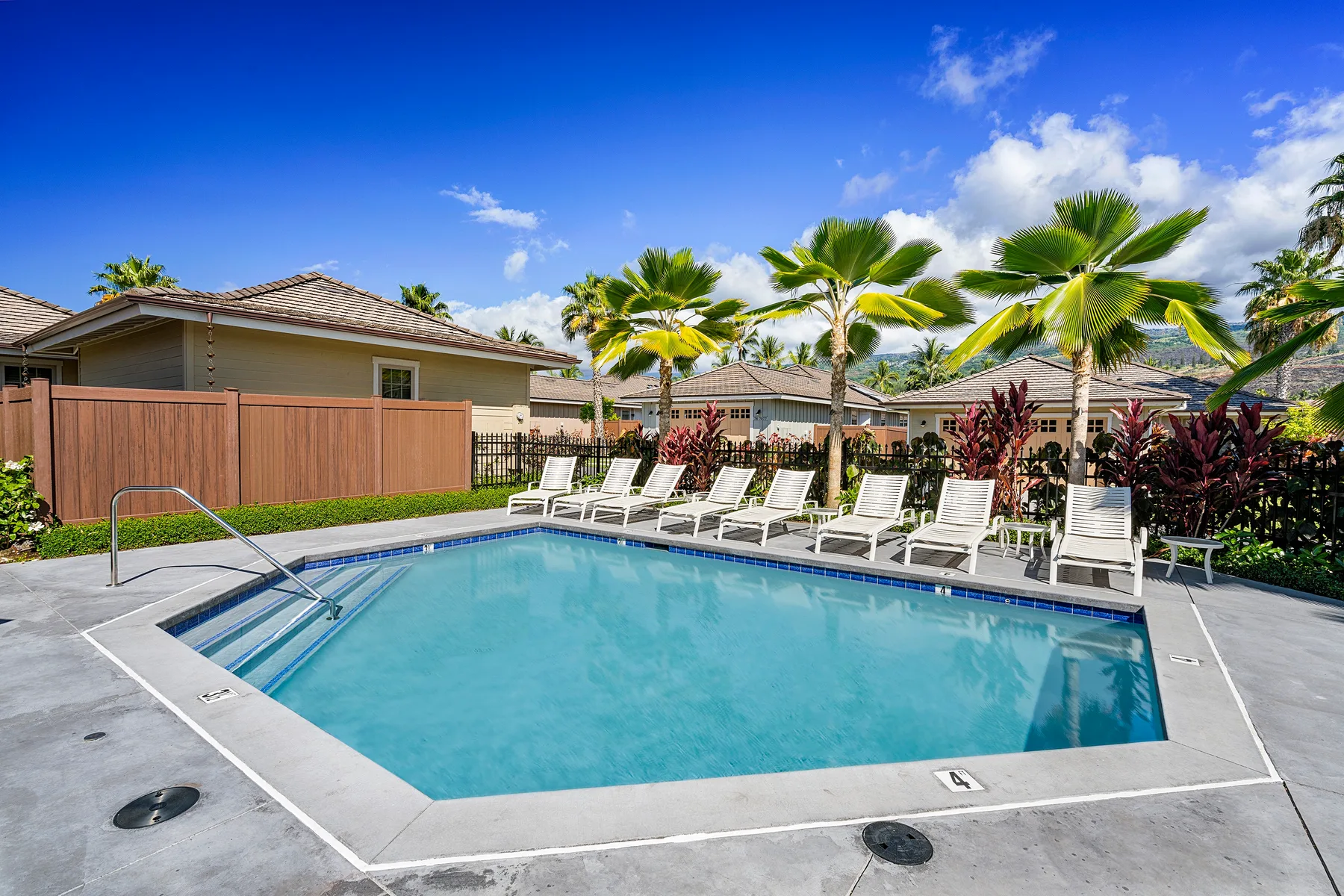 A bright outdoor swimming pool is surrounded by lounge chairs and palm trees.