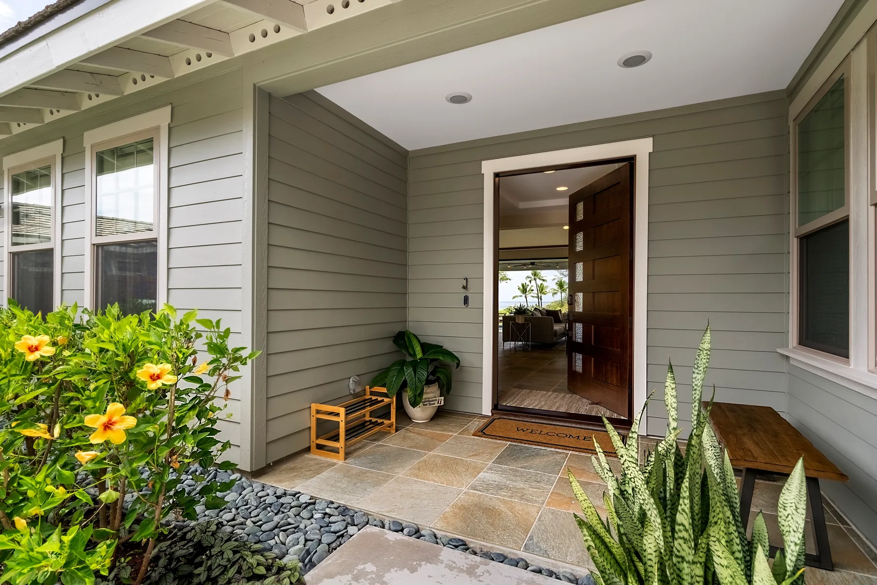 A covered entrance patio with an open doorway and potted greenery.