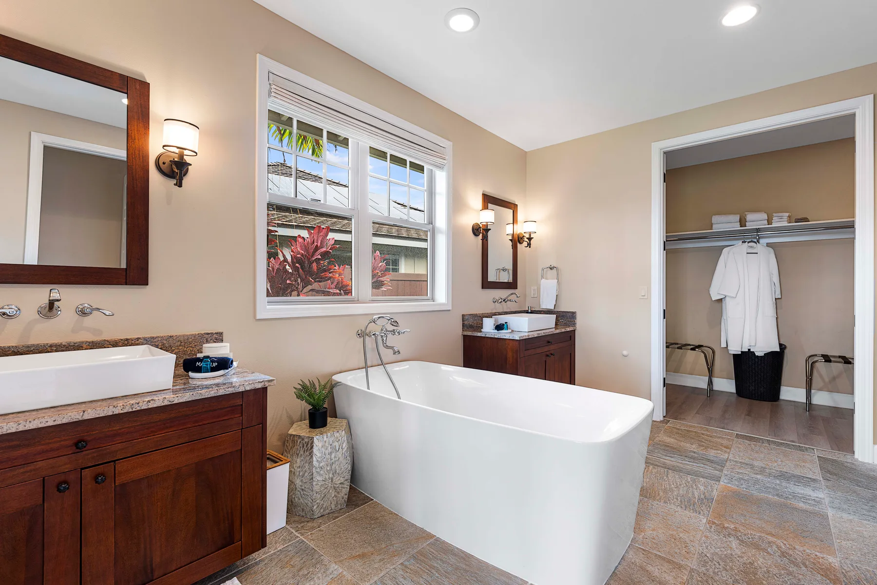 A bathroom with a freestanding bathtub, wooden vanity, and an open closet.