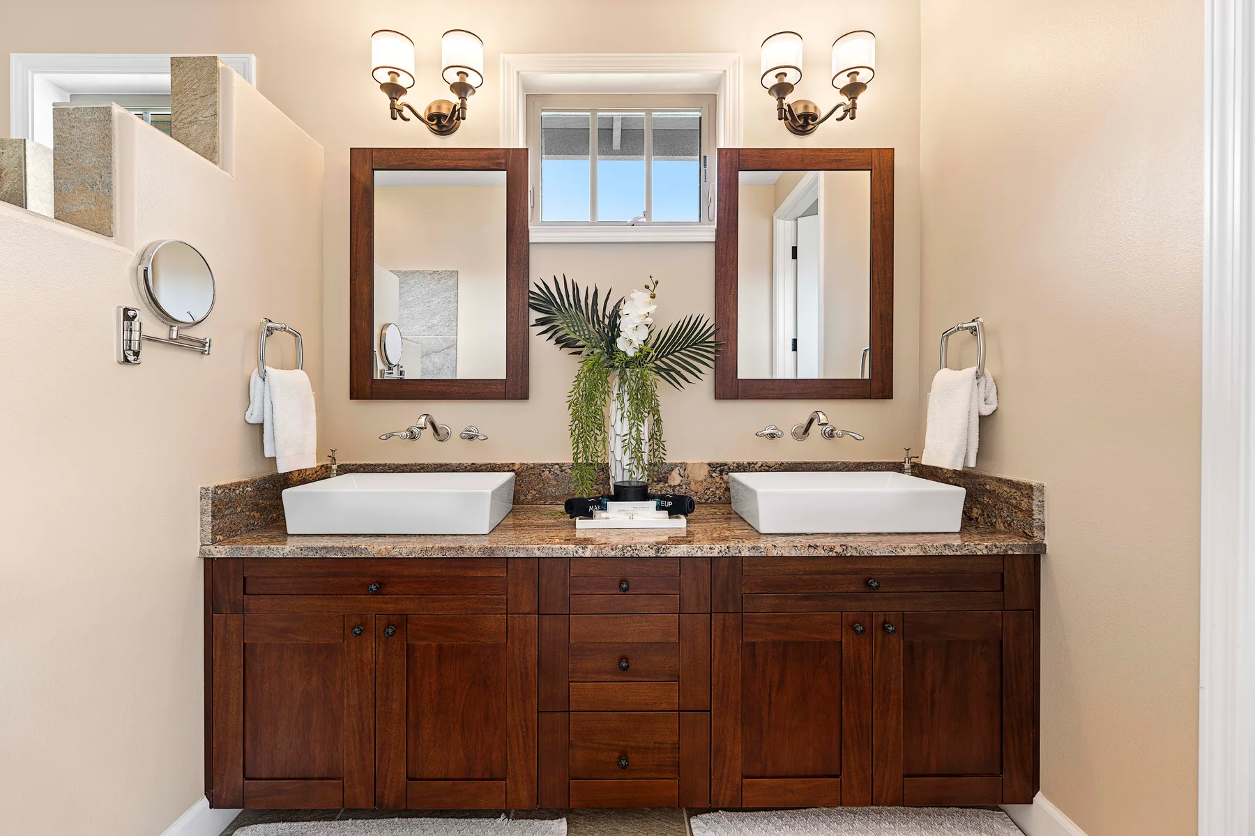 A bathroom vanity with two sinks sits beneath mirrors and wall lights.