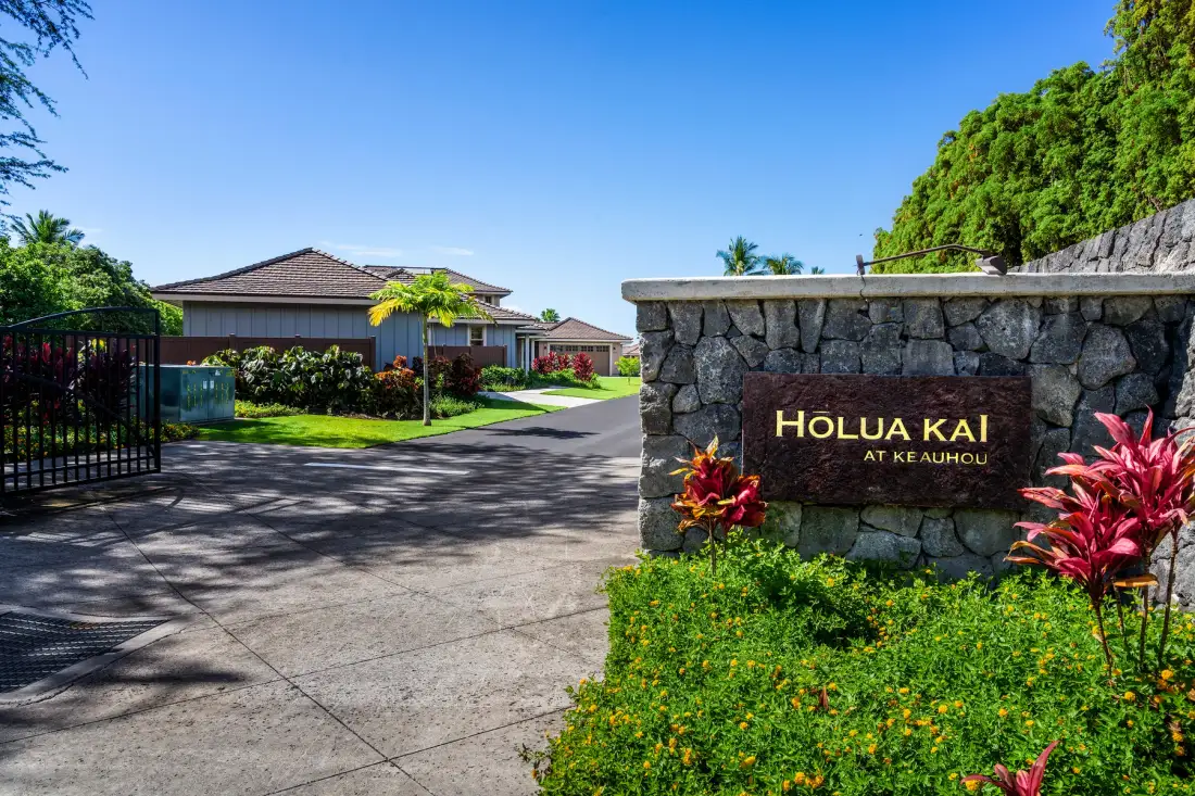 A gated residential entrance with a stone sign and landscaped greenery.