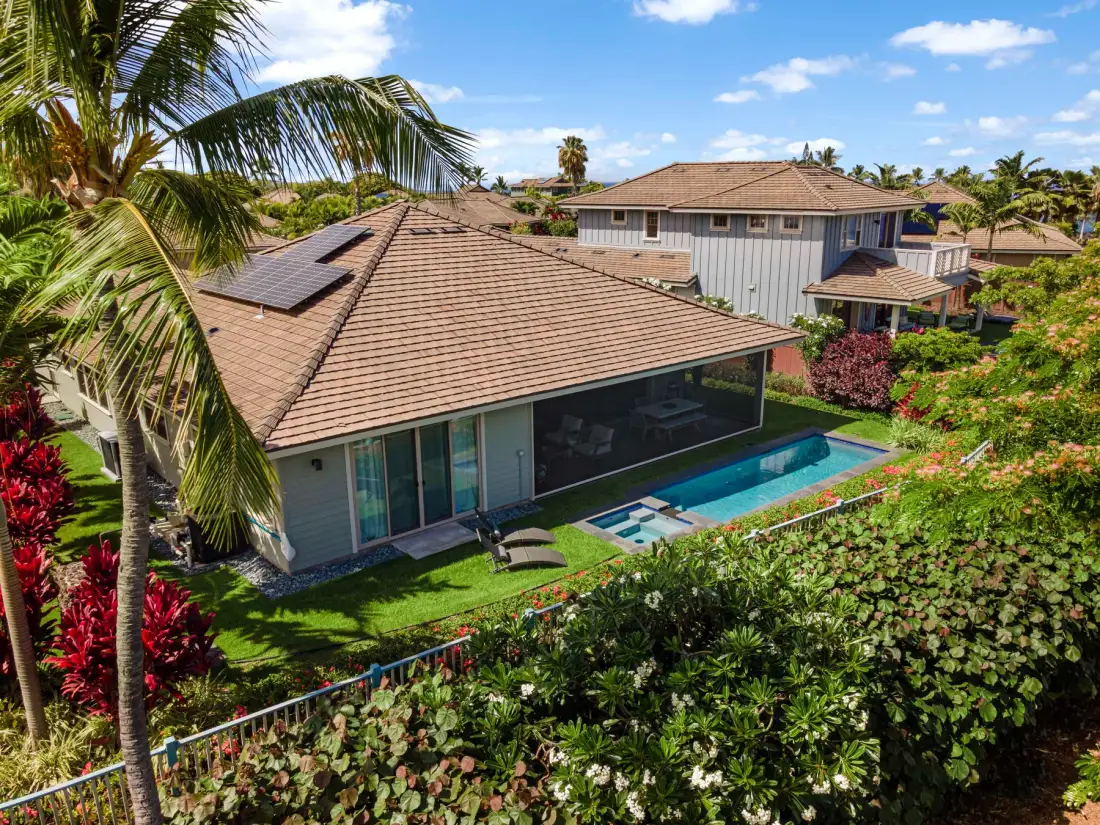 A house with a swimming pool is surrounded by tropical landscaping.