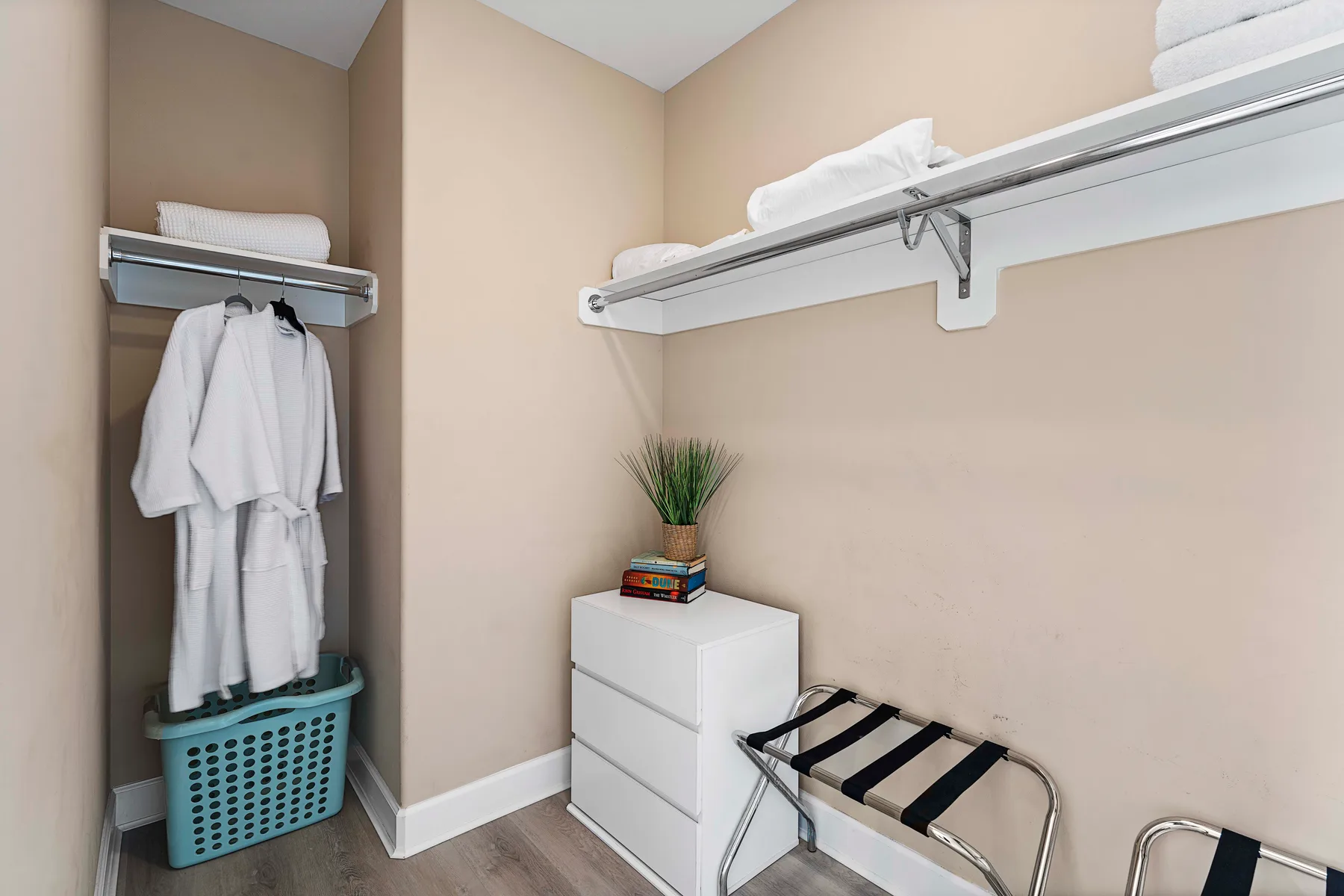 A bedroom closet area with hanging robes, folded towels, and a dresser.