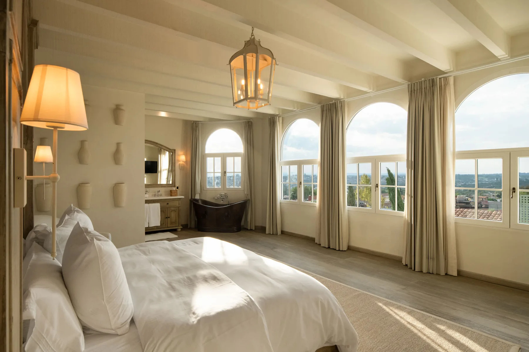 A bright bedroom with a bed beside tall windows overlooking the sea.