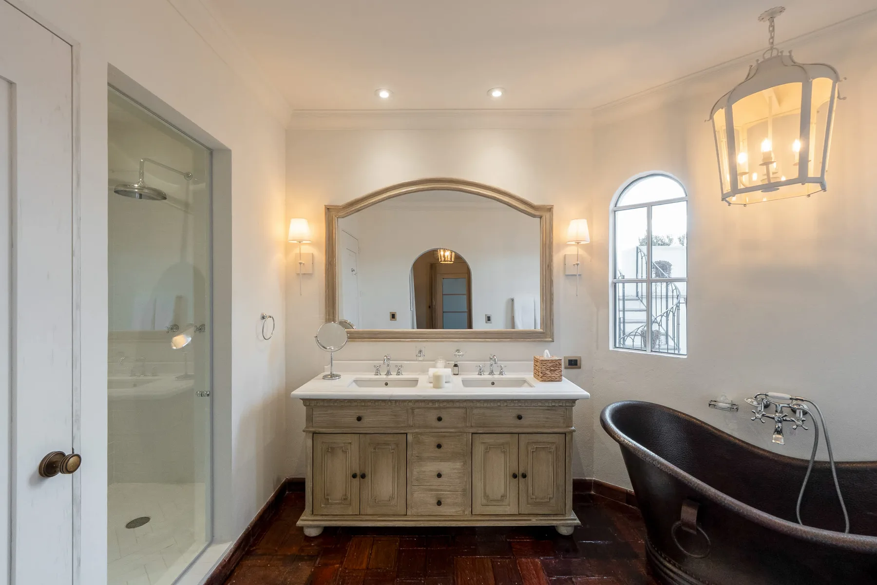 Un baño luminoso cuenta con un lavabo doble, un espejo grande y una bañera exenta.