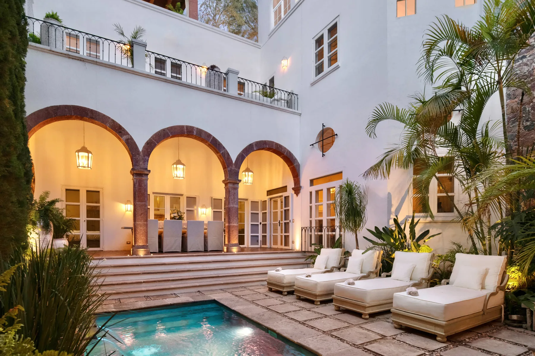 Una piscina en un patio junto a arcos y asientos al aire libre.