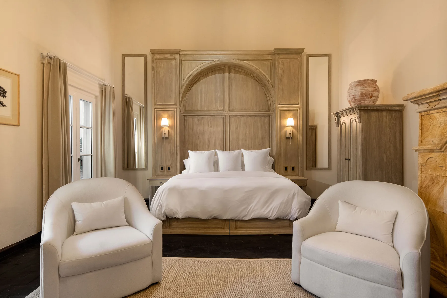 A bedroom with a white bed and two upholstered chairs in the foreground.