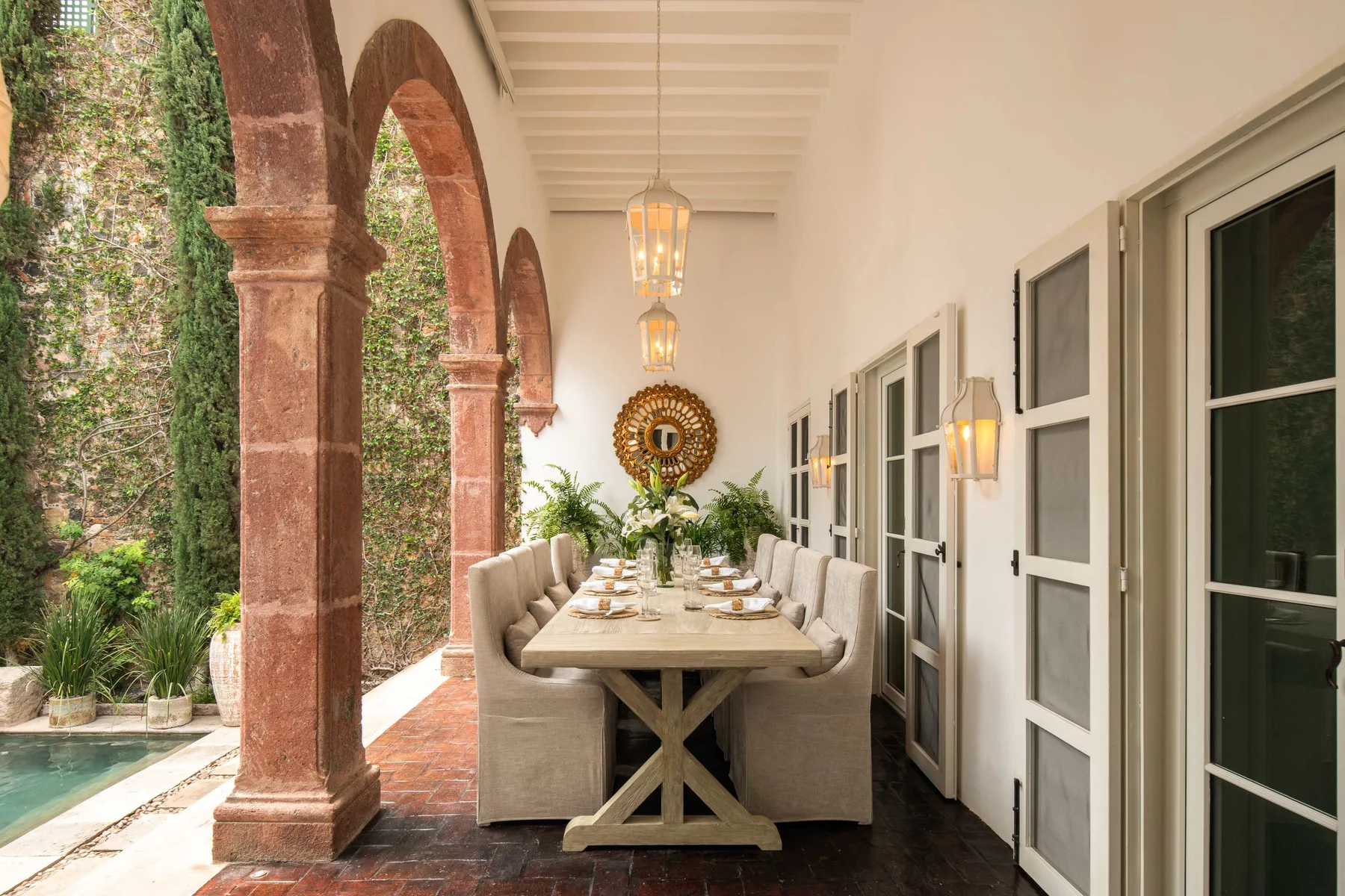 Comedor exterior cubierto con una mesa larga junto a columnas de piedra arqueadas.