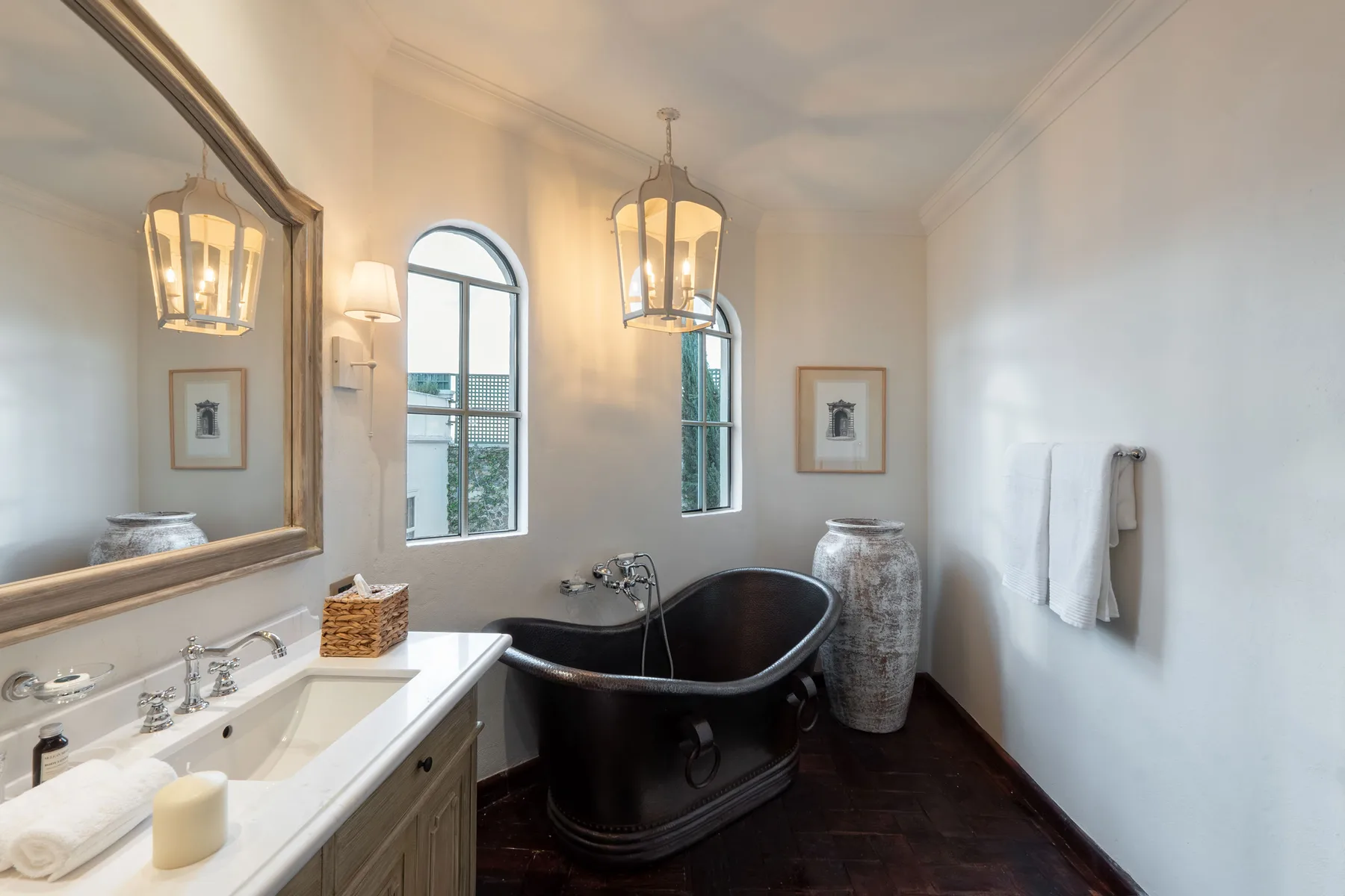 Un baño luminoso con bañera exenta, lavabo y ventanas altas arqueadas.