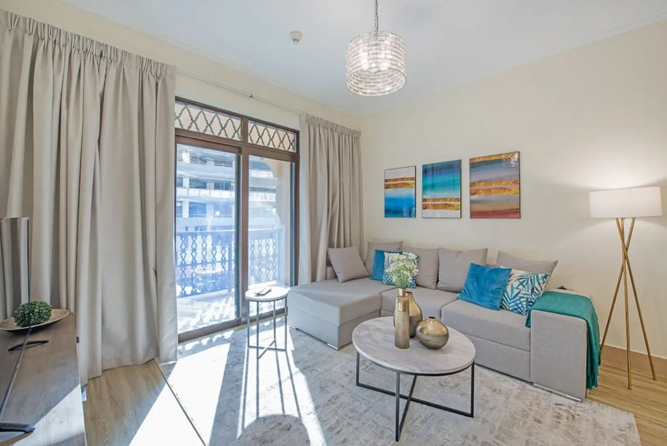 A bright living room with light seating, colorful wall art, and a glass balcony door.