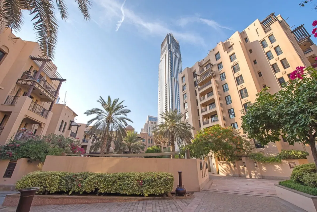 A landscaped courtyard with palm trees and tall buildings under a blue sky.