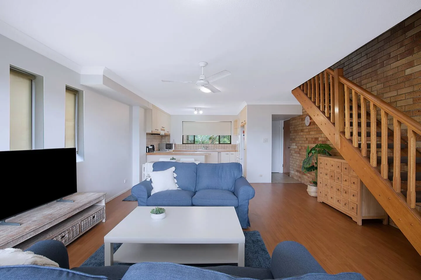 Una sala de estar con asientos azules, un televisor y una escalera de madera.