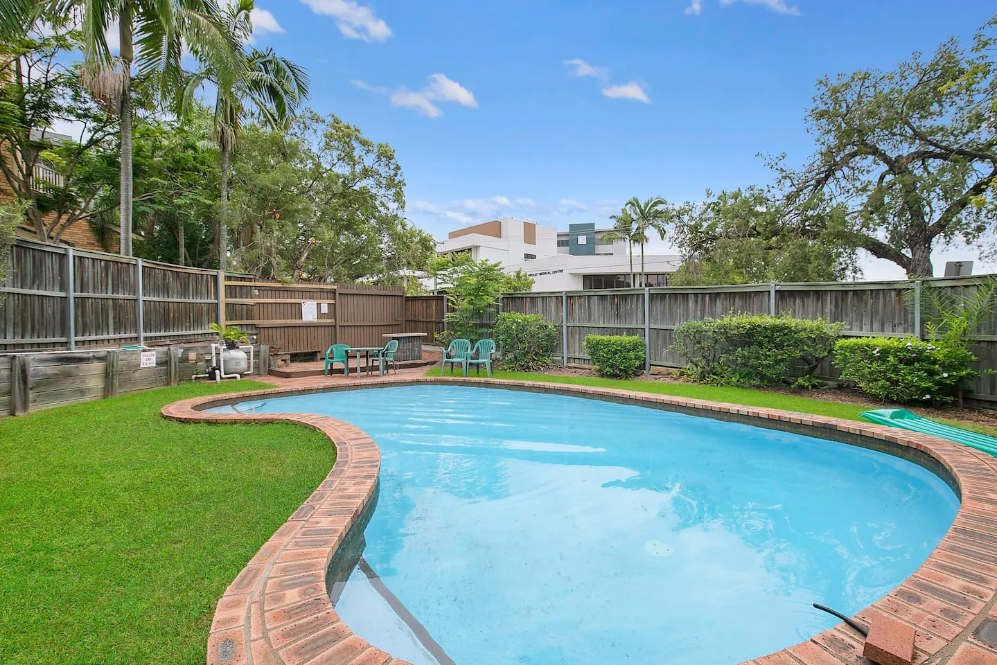 Una piscina en el patio se curva junto a un césped y asientos de exterior.