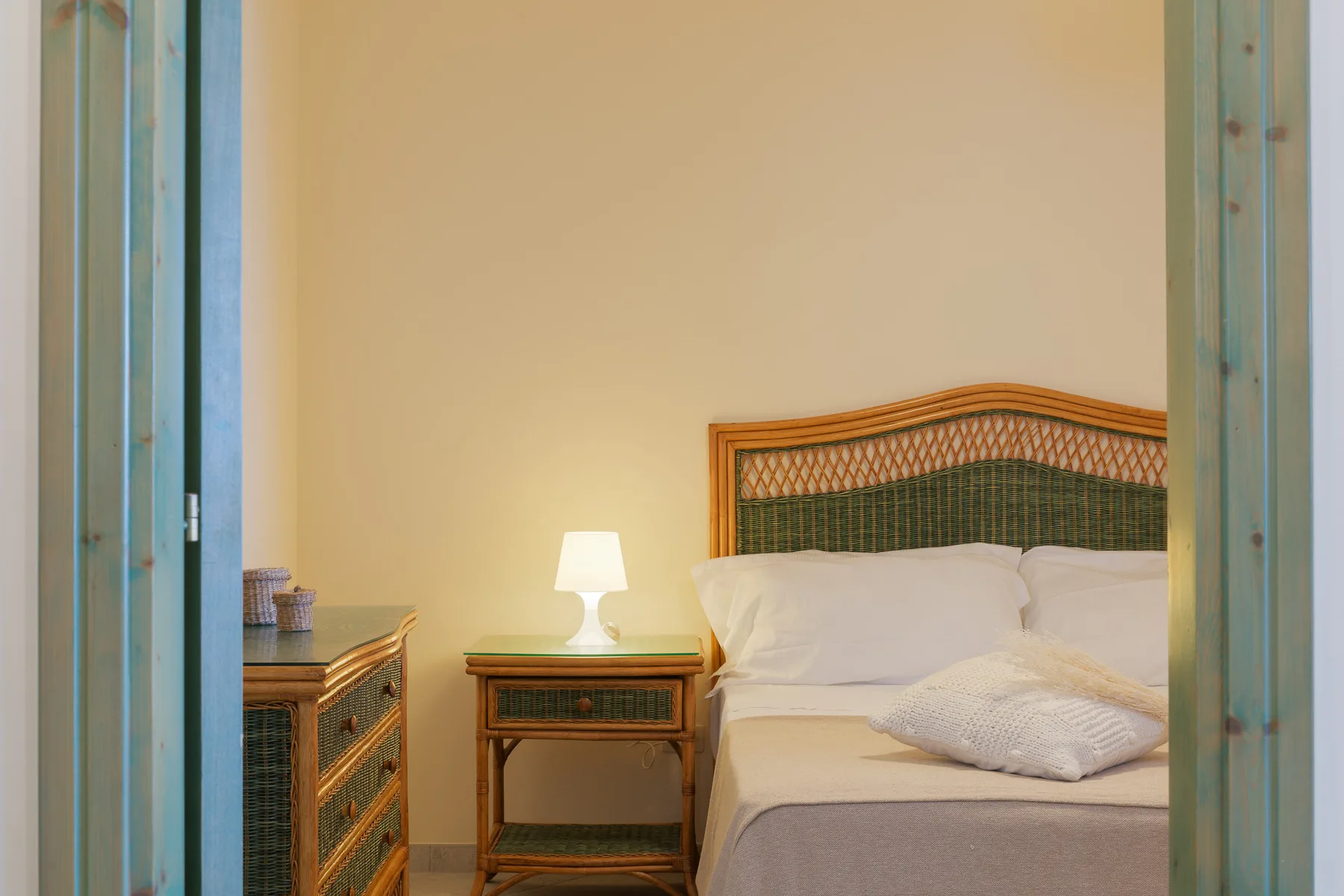 A bedroom with a bed, a bedside table, and a lit lamp.