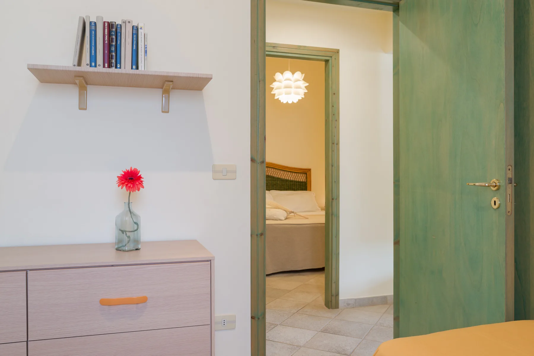 A bedroom doorway opens beside a dresser topped with a vase and flower.