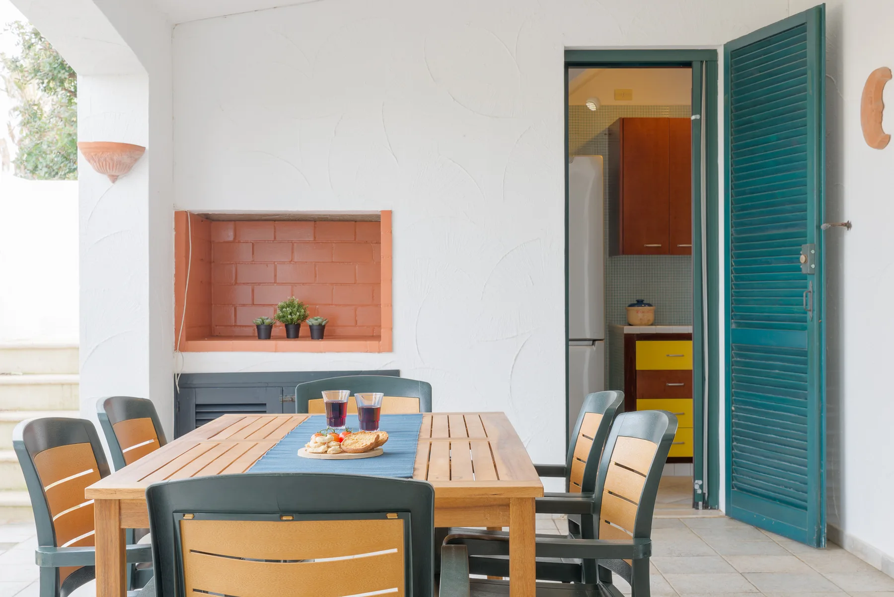 A dining area with a wooden table and teal chairs beside an open doorway.