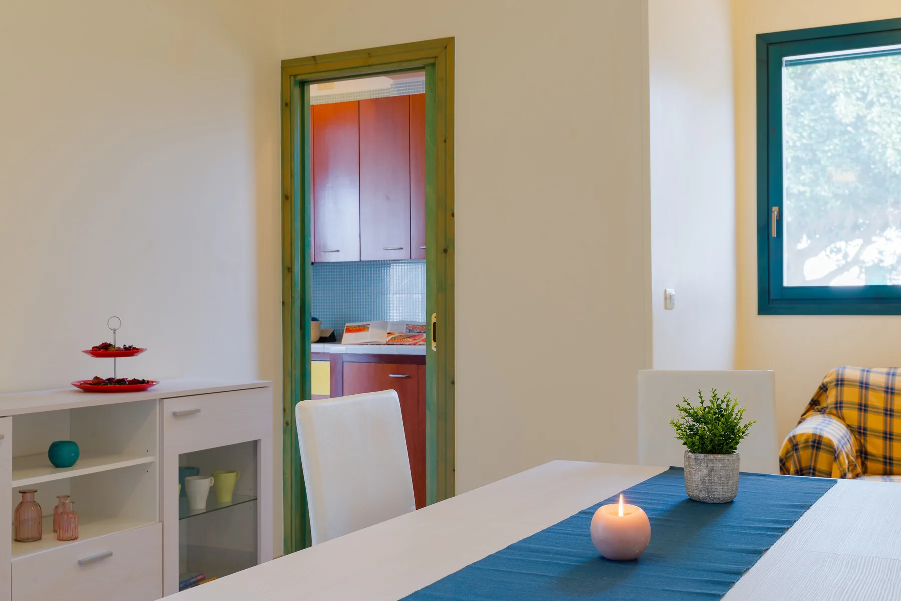 A dining area with a table, blue runner, and a window overlooking trees.