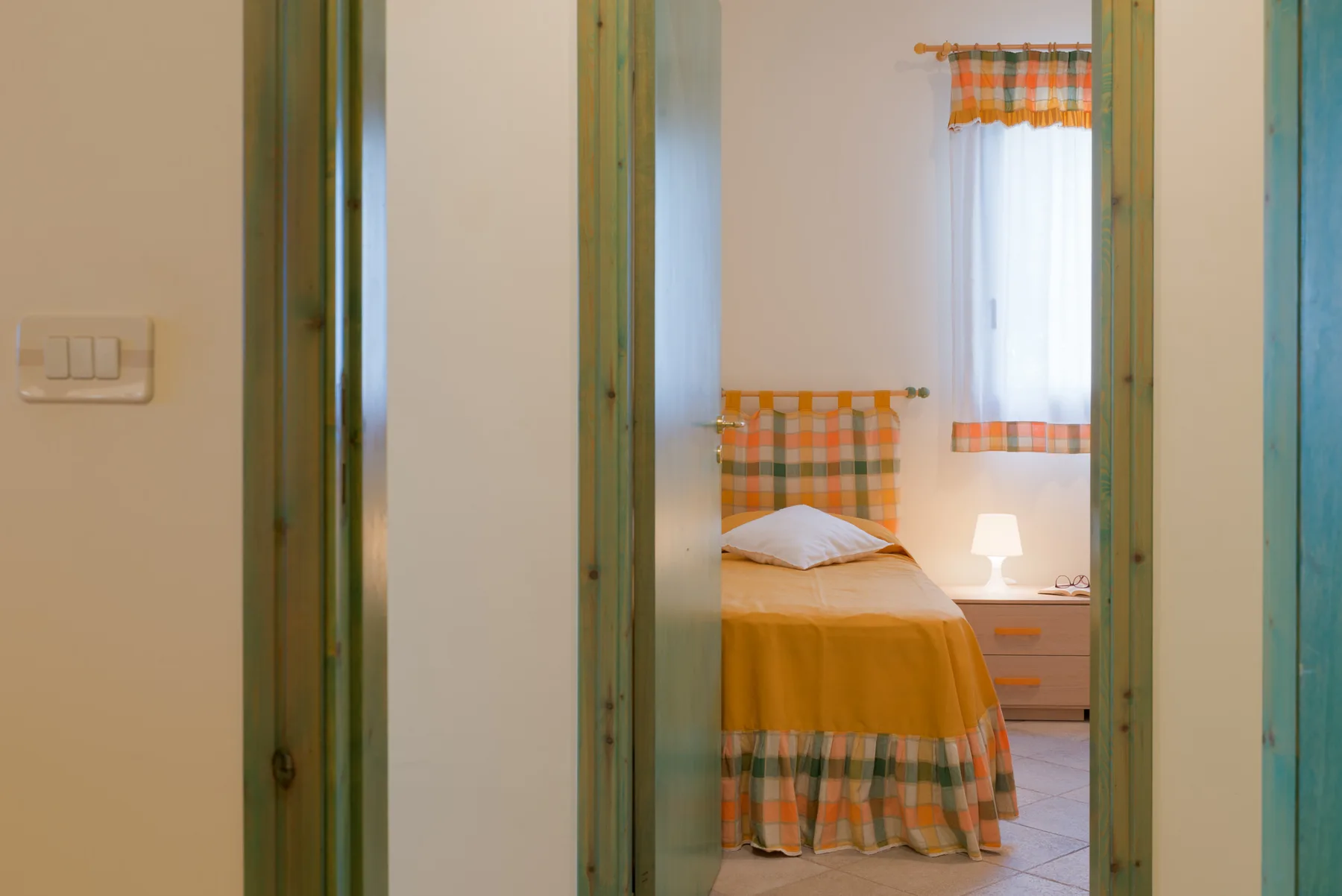 A bedroom is visible through an open doorway, with a bed beside a window.