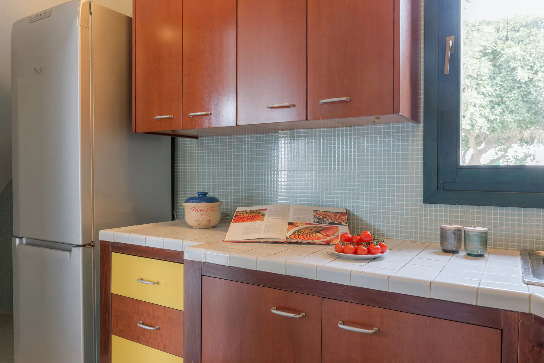 A kitchen counter beneath wooden cabinets holds cookbooks, a bowl, and small containers.